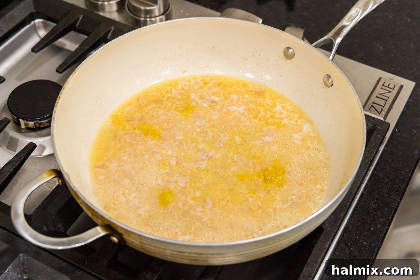 The white wine sauce for the pasta simmering in the skillet, infused with garlic, shallots, and lemon zest.