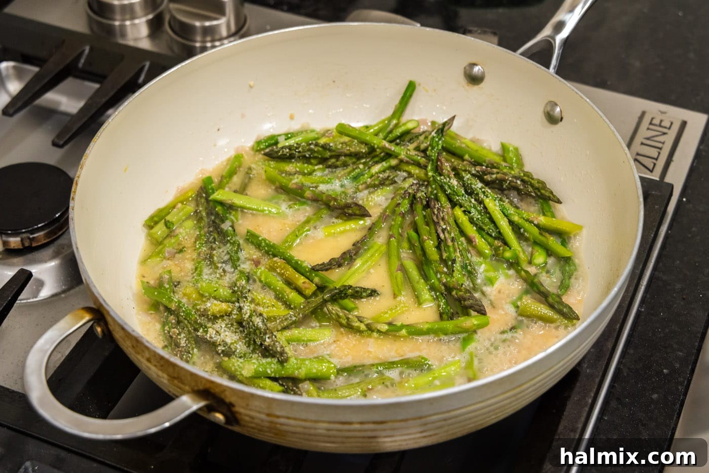 Fresh asparagus spears added to the simmering butter, garlic, shallot, and white wine mixture in the skillet.