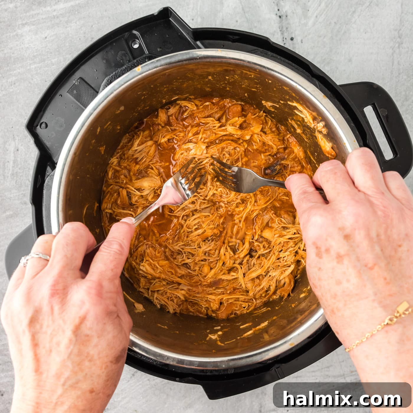 Shredding barbecue chicken directly in the Instant Pot with two forks.