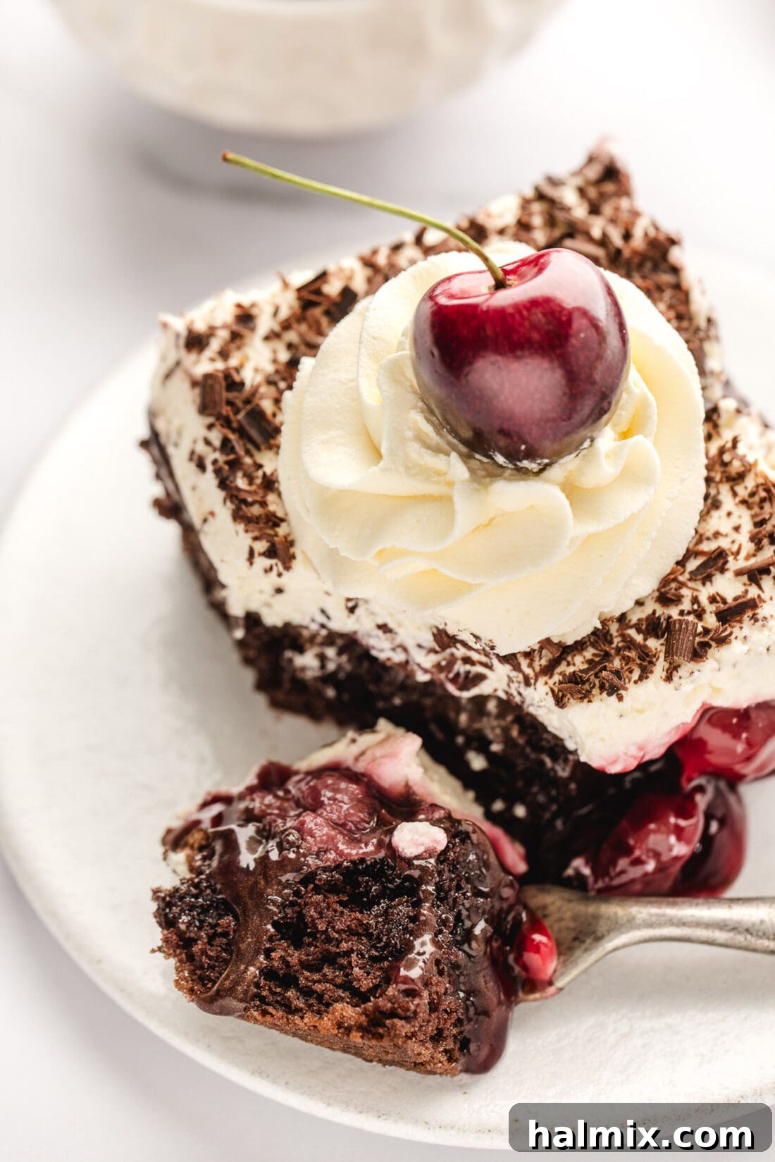 Decadent Black Forest Poke Cake 12 Piece of Black Forest Poke Cake on a plate with a bite removed on a fork