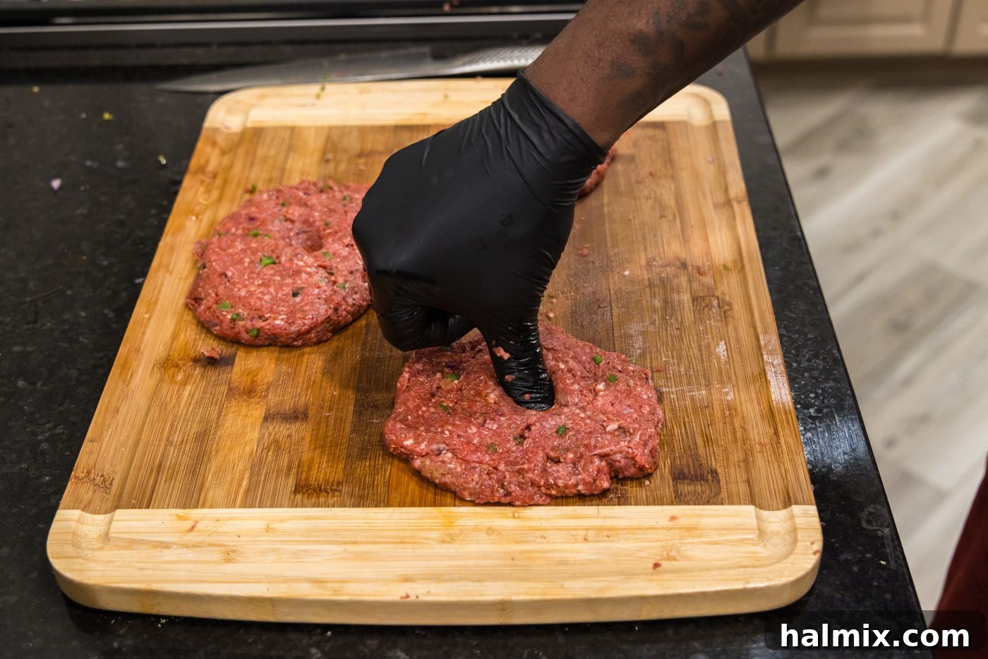 Mighty Buffalo Burger 9 A thumb pressing into the center of a bison burger patty to create an indent, preparing it for even cooking.