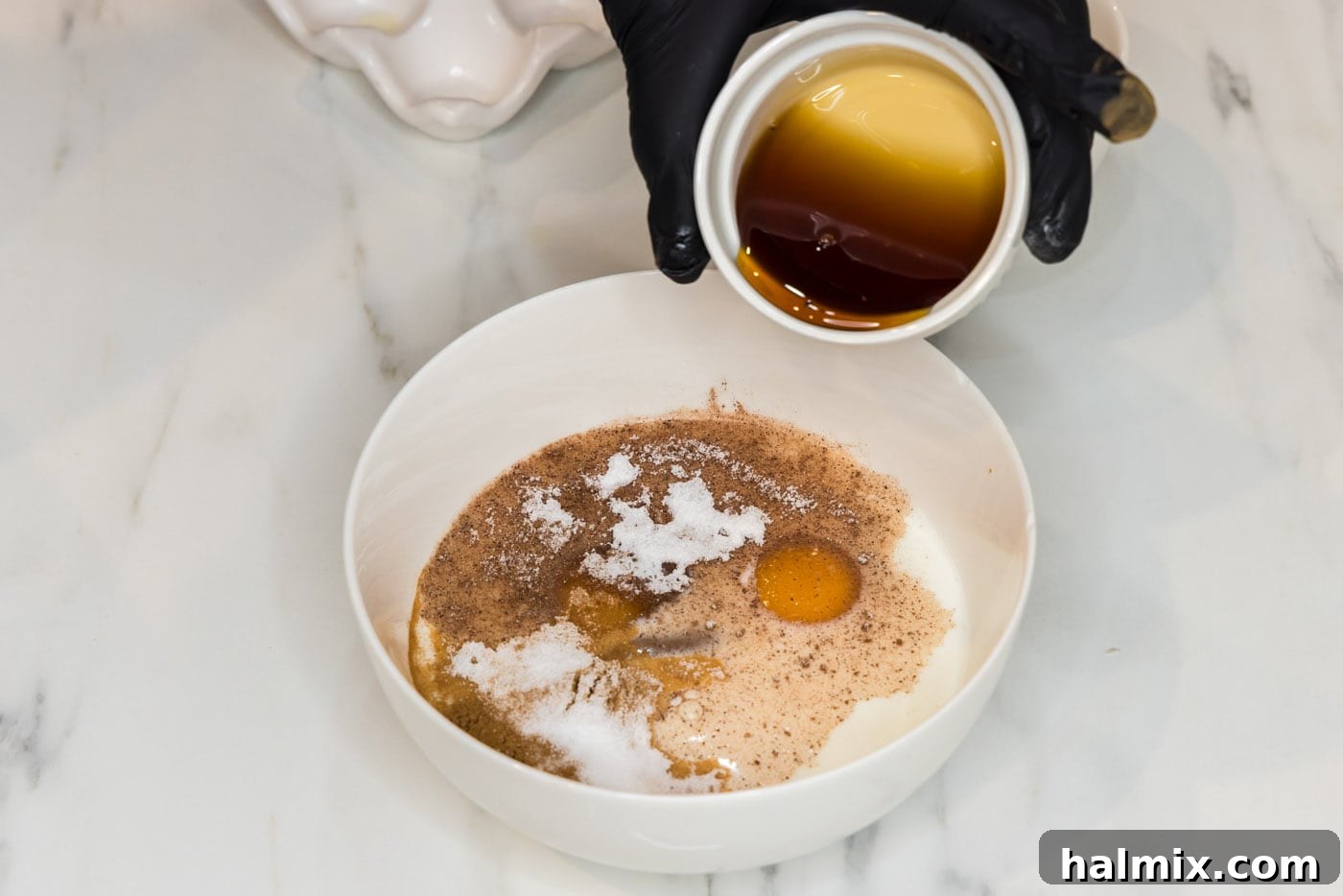 hand pouring maple syrup into French toast batter in a bowl