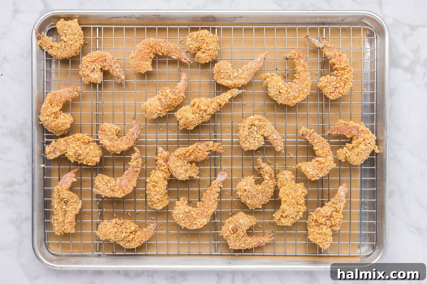 All breaded shrimp neatly arranged on a baking sheet with a wire rack