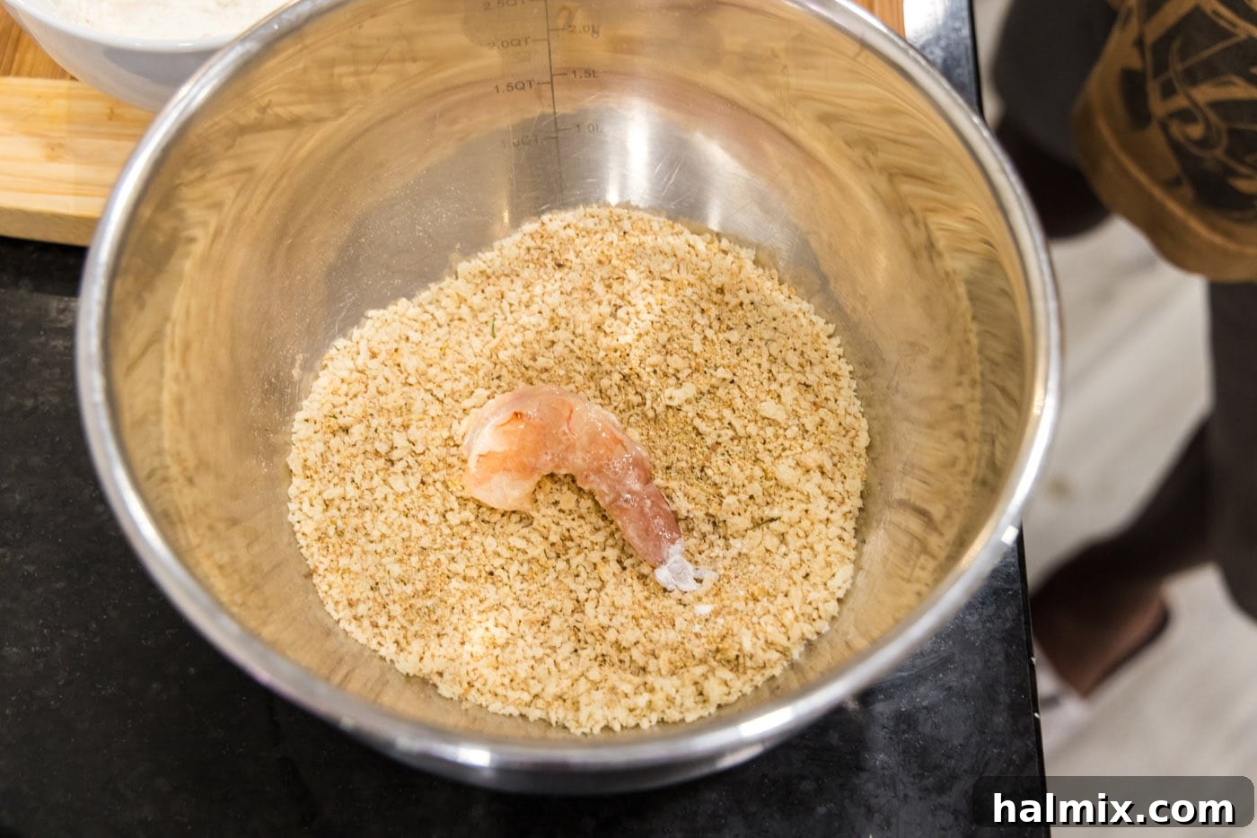 Dredged shrimp being pressed into the breadcrumb mixture for a full coating