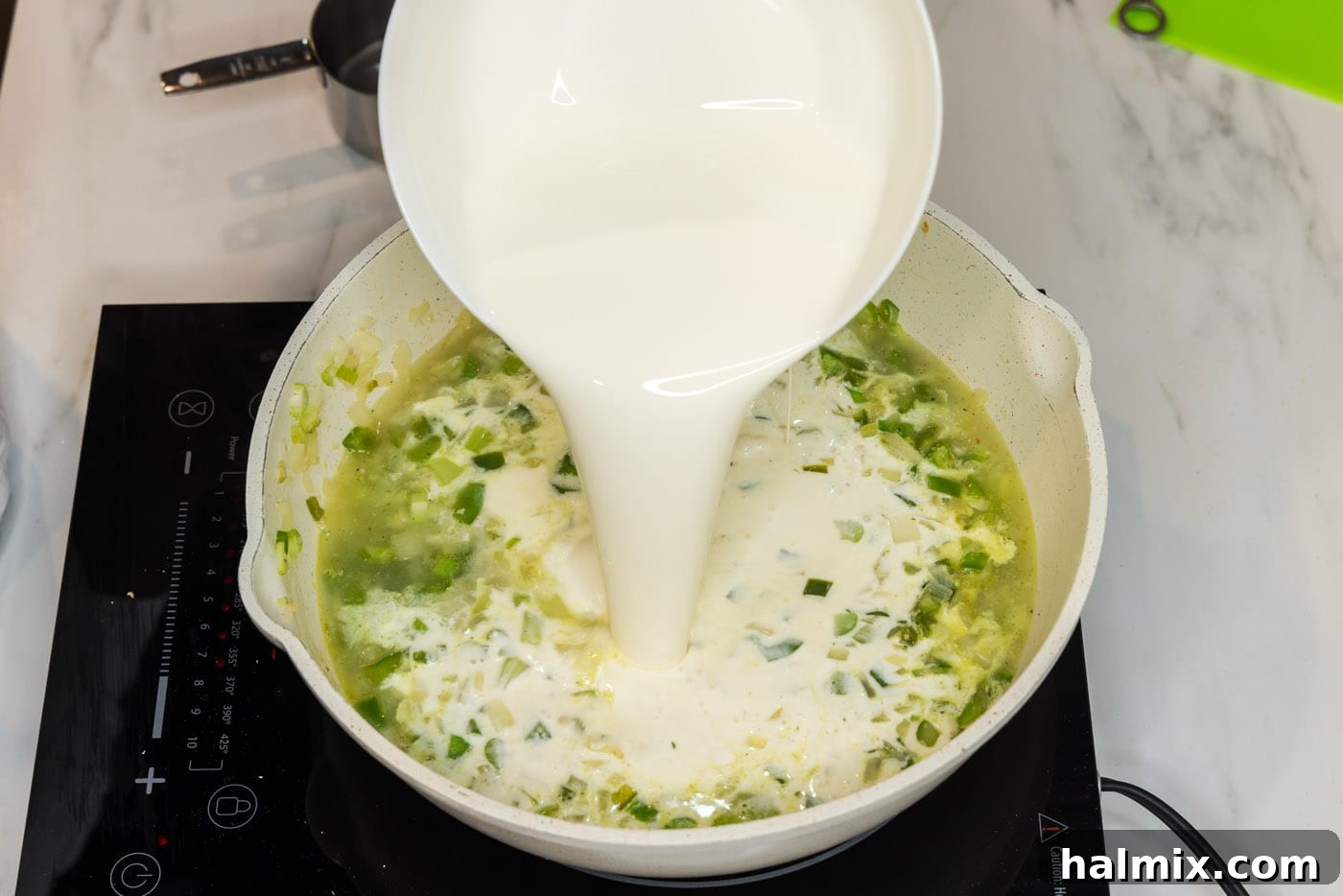 Pouring heavy cream into the skillet with sautéed vegetables and stock