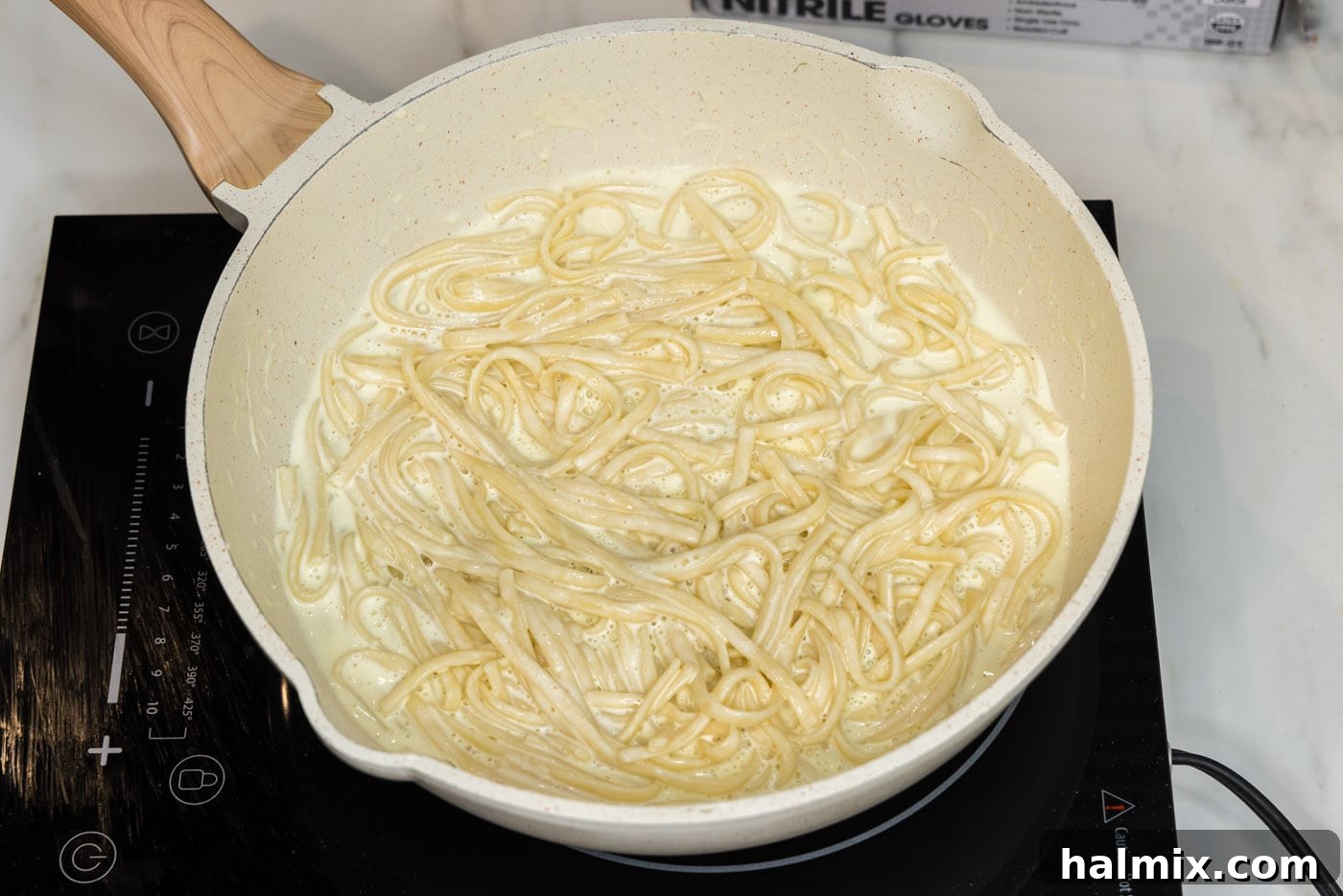 Linguine noodles and lobster chunks being tossed into the creamy sauce in a skillet