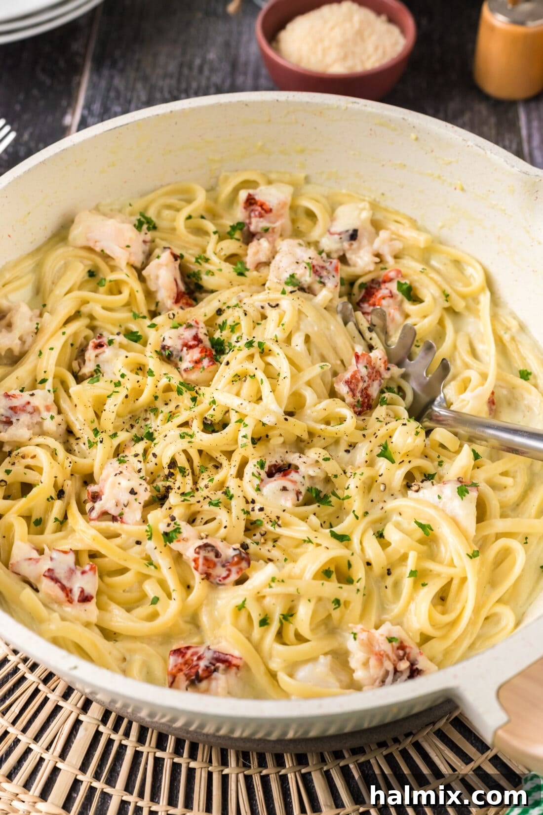 Creamy lobster pasta simmering in a deep skillet with a serving spoon