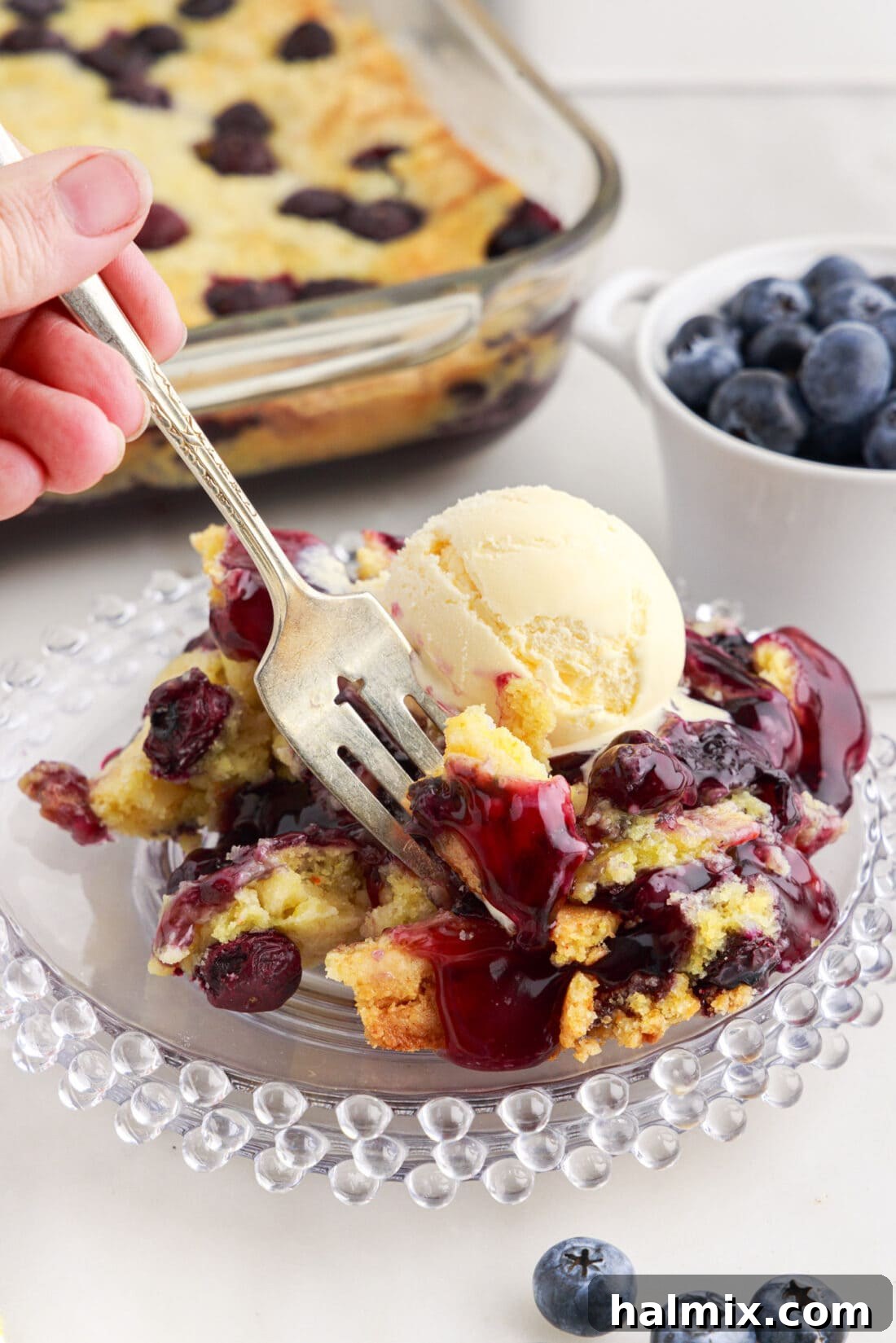 Blueberry Crumble Bake 3 Fork dipping into a serving of Blueberry Dump Cake on a white plate, highlighting the tender cake and juicy blueberries