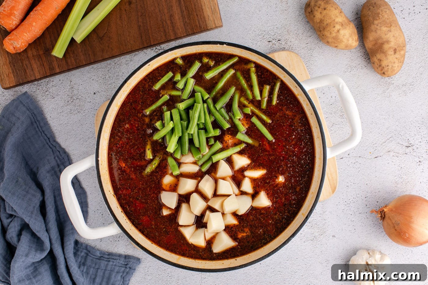 Adding potatoes and green beans to the simmering vegetable beef soup.
