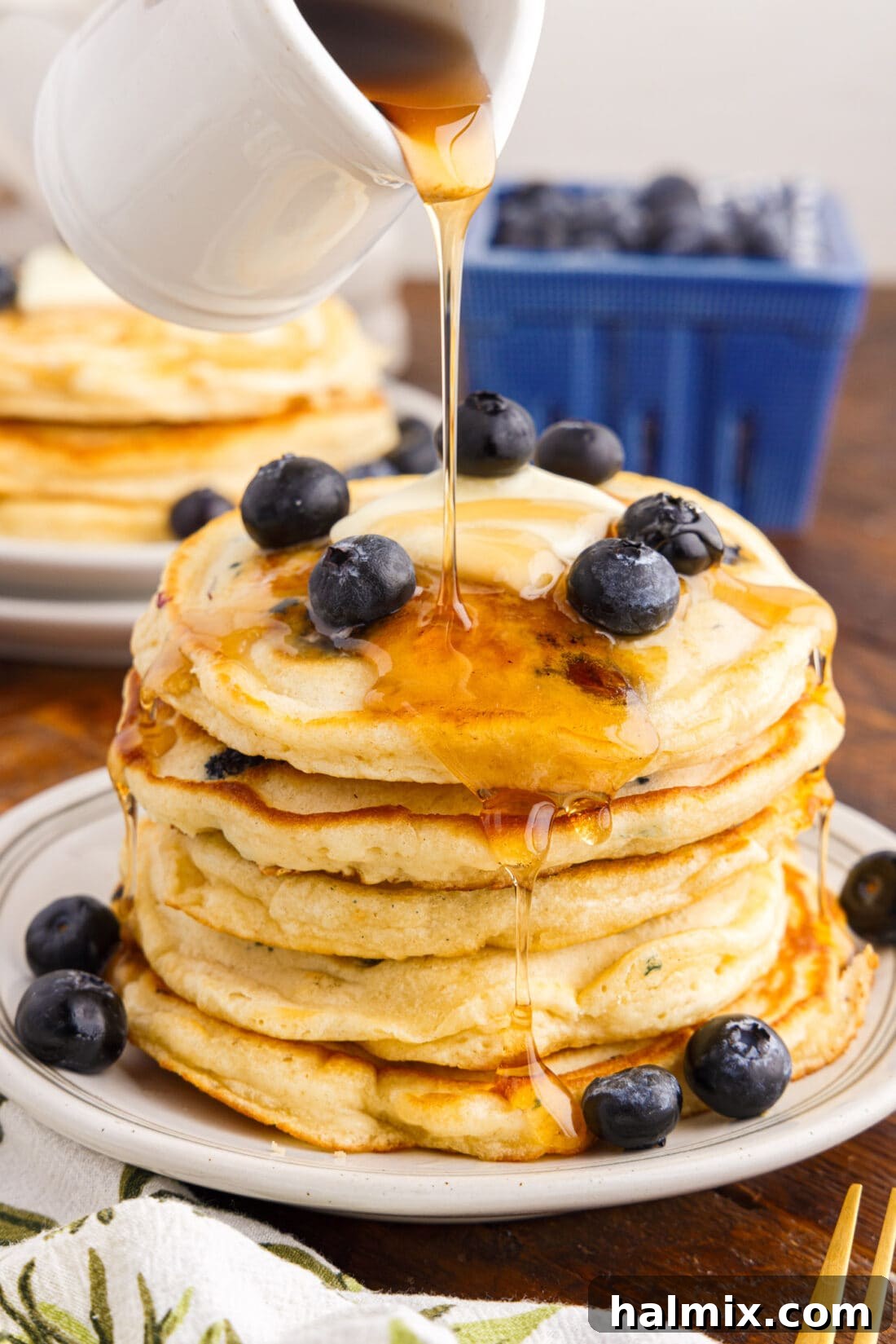 Syrup being poured over a stack of fluffy blueberry pancakes