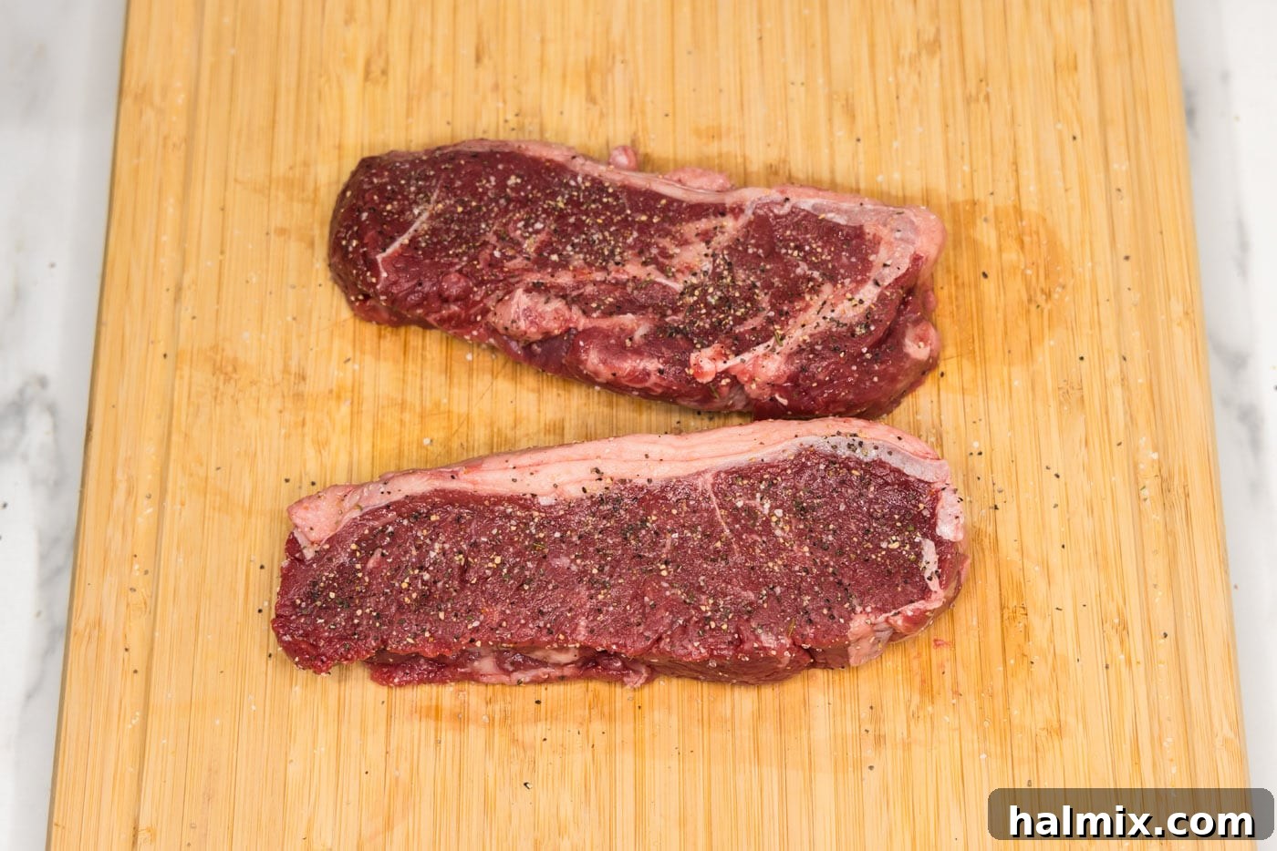 Seasoned New York strip steaks ready for sous vide on a cutting board