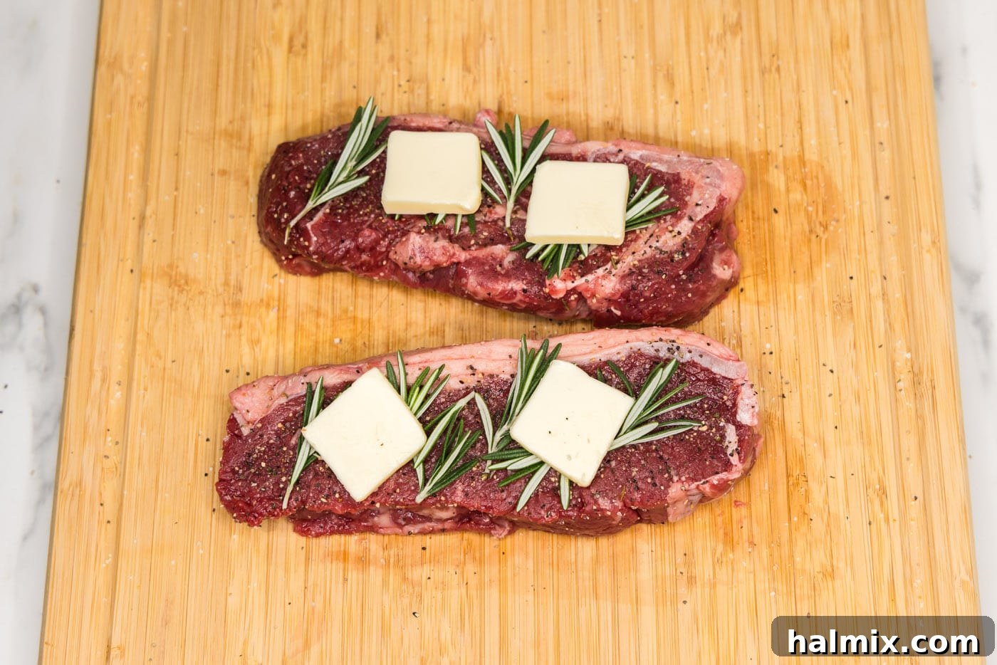 New York strip steaks topped with fresh rosemary and pats of butter