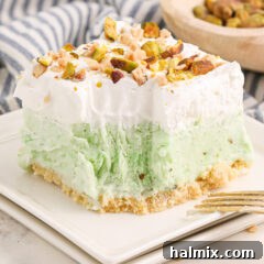 Close up photo of a square of Pistachio Ice Cream Cake on a plate with a bite removed, showcasing the perfect layers.