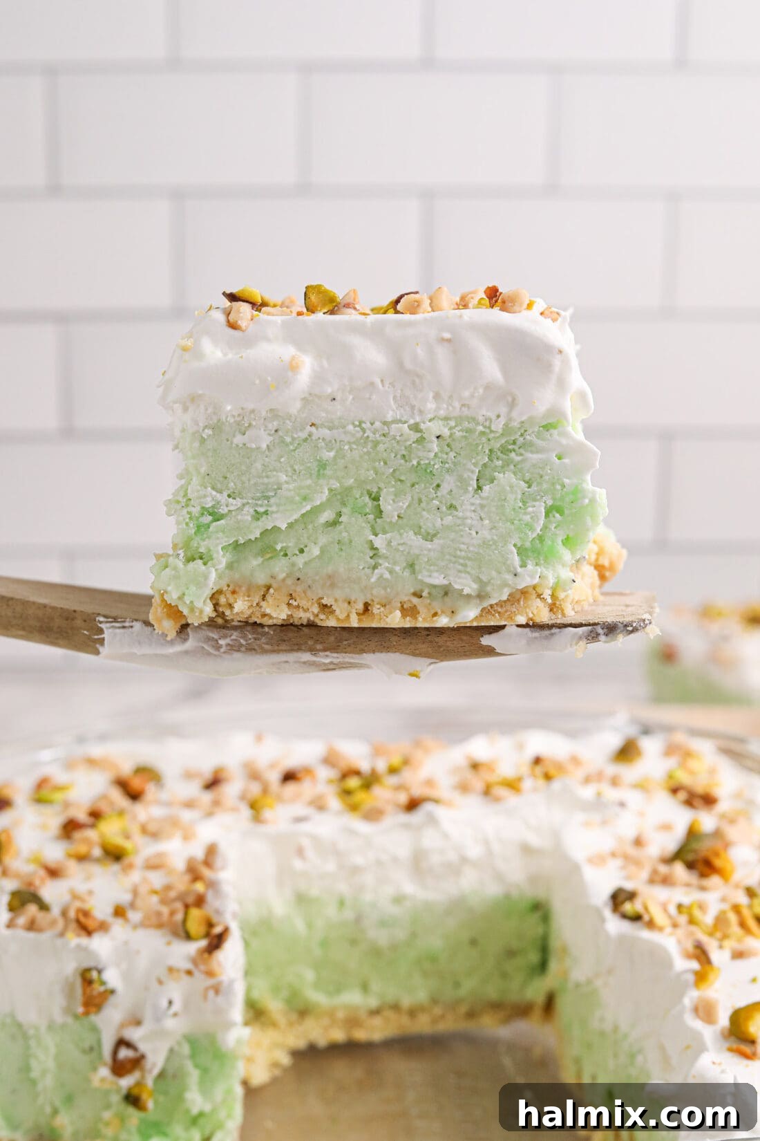 A wide spatula lifting a perfect slice of homemade Pistachio Ice Cream Cake out of a square baking pan, showcasing its rich, layered texture.