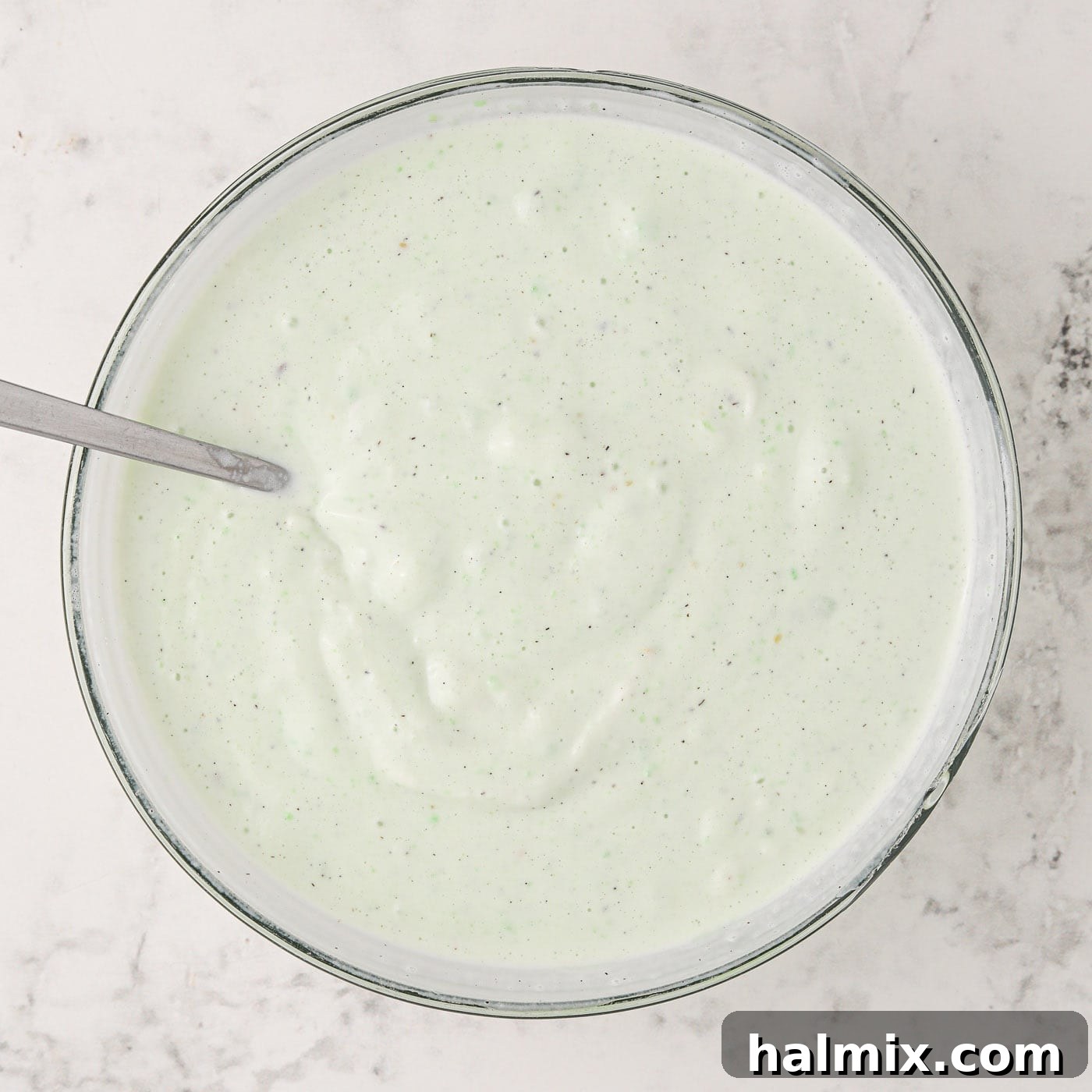 Softened vanilla ice cream being folded into the pistachio pudding mix in a bowl.