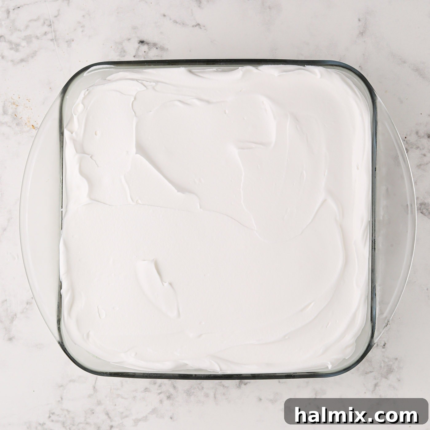 Whipped topping smoothly spread over the pistachio ice cream layer in the baking dish.