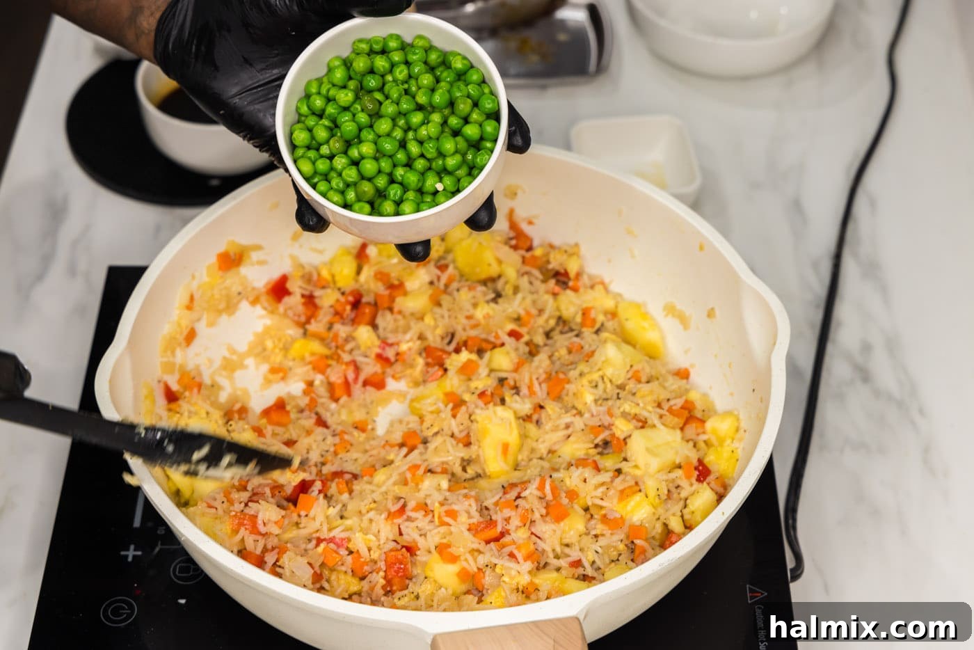 Frozen peas being added to a skillet with fried rice and other ingredients.