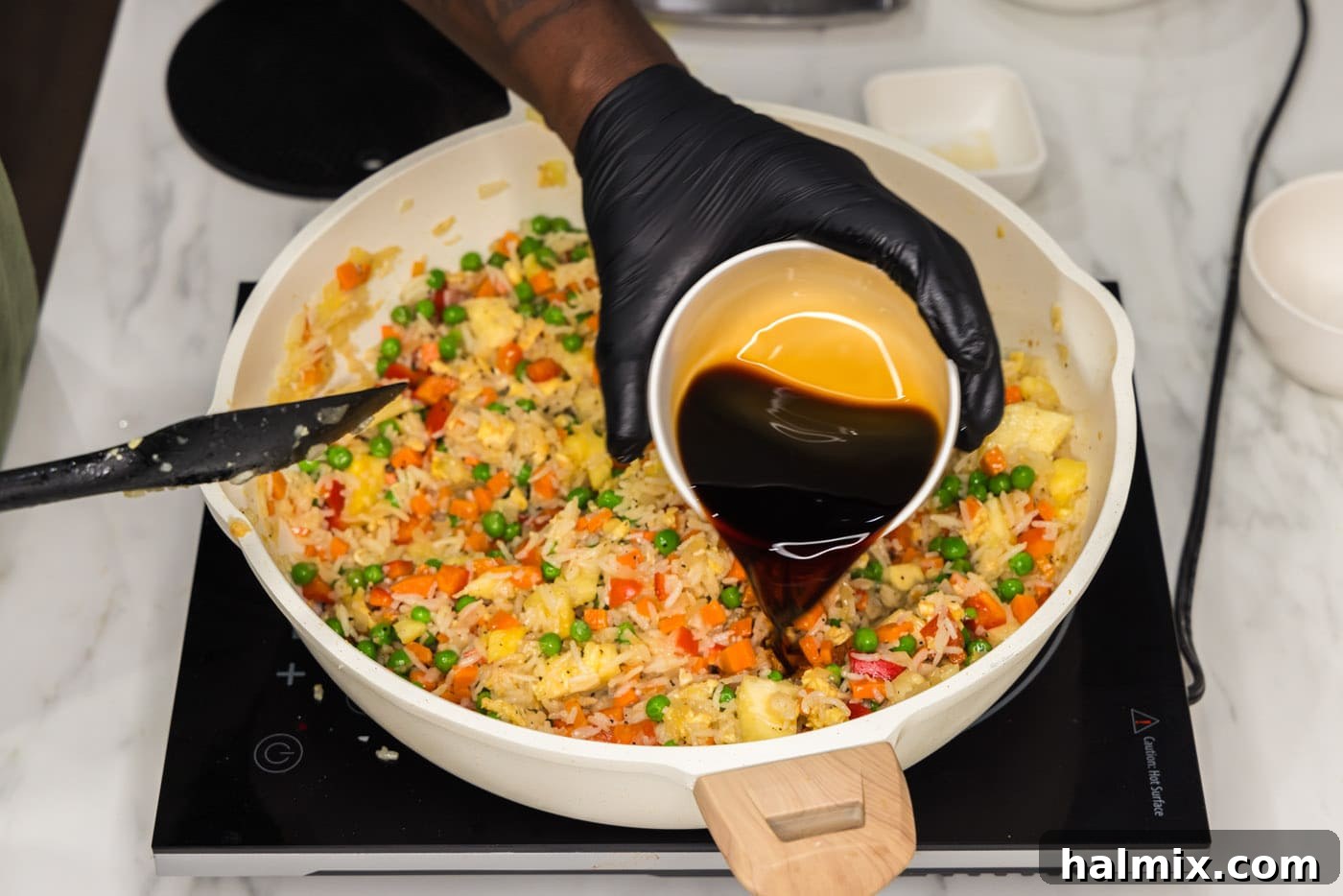 Soy sauce being poured into a skillet containing pineapple fried rice.