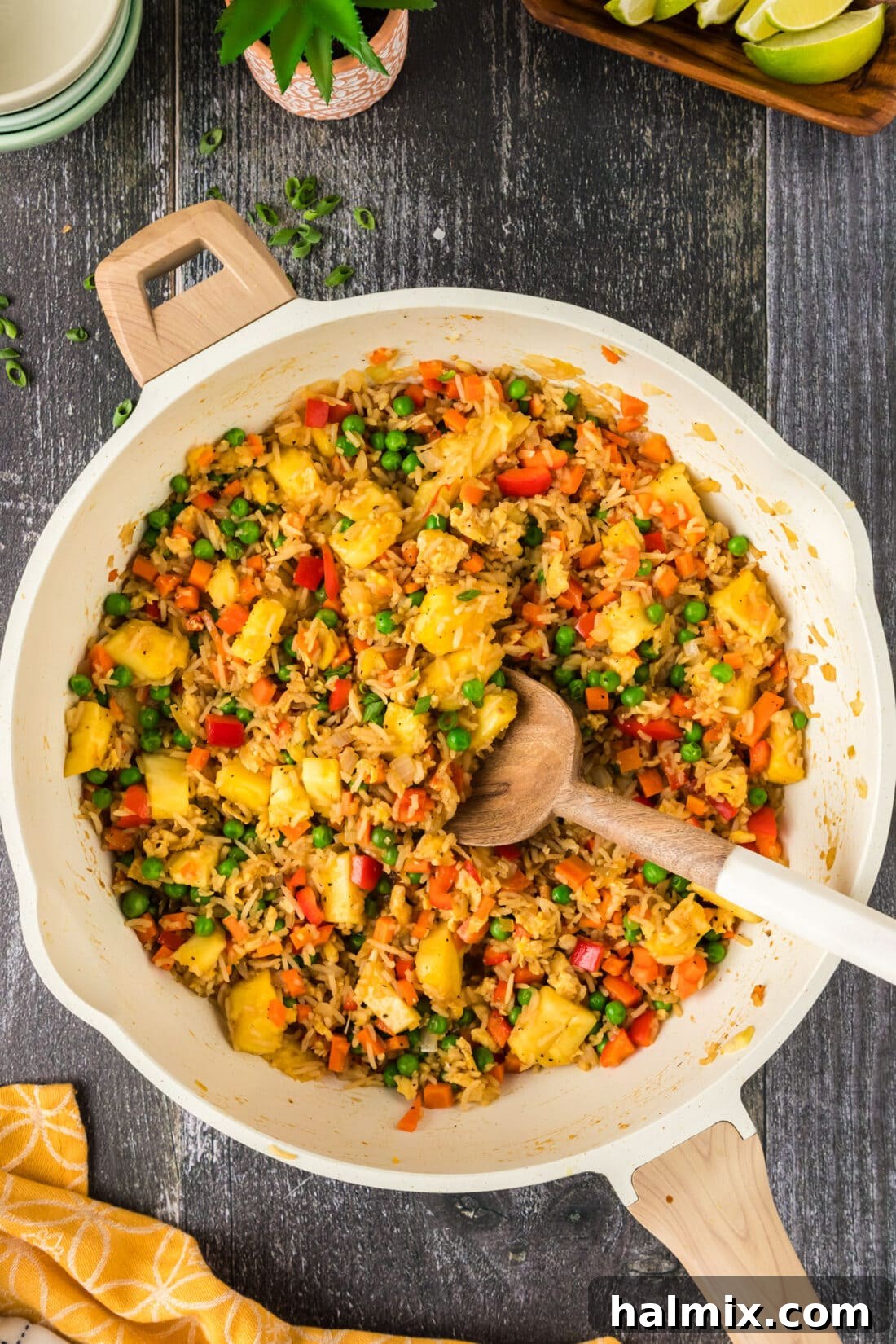 Close-up of Pineapple Fried Rice being stirred in a large skillet with a wooden spoon, showcasing colorful ingredients.