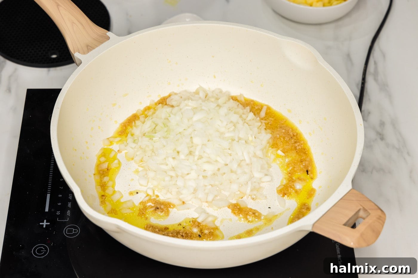 Diced onion added to a skillet with garlic, ginger, and olive oil, sautéing.