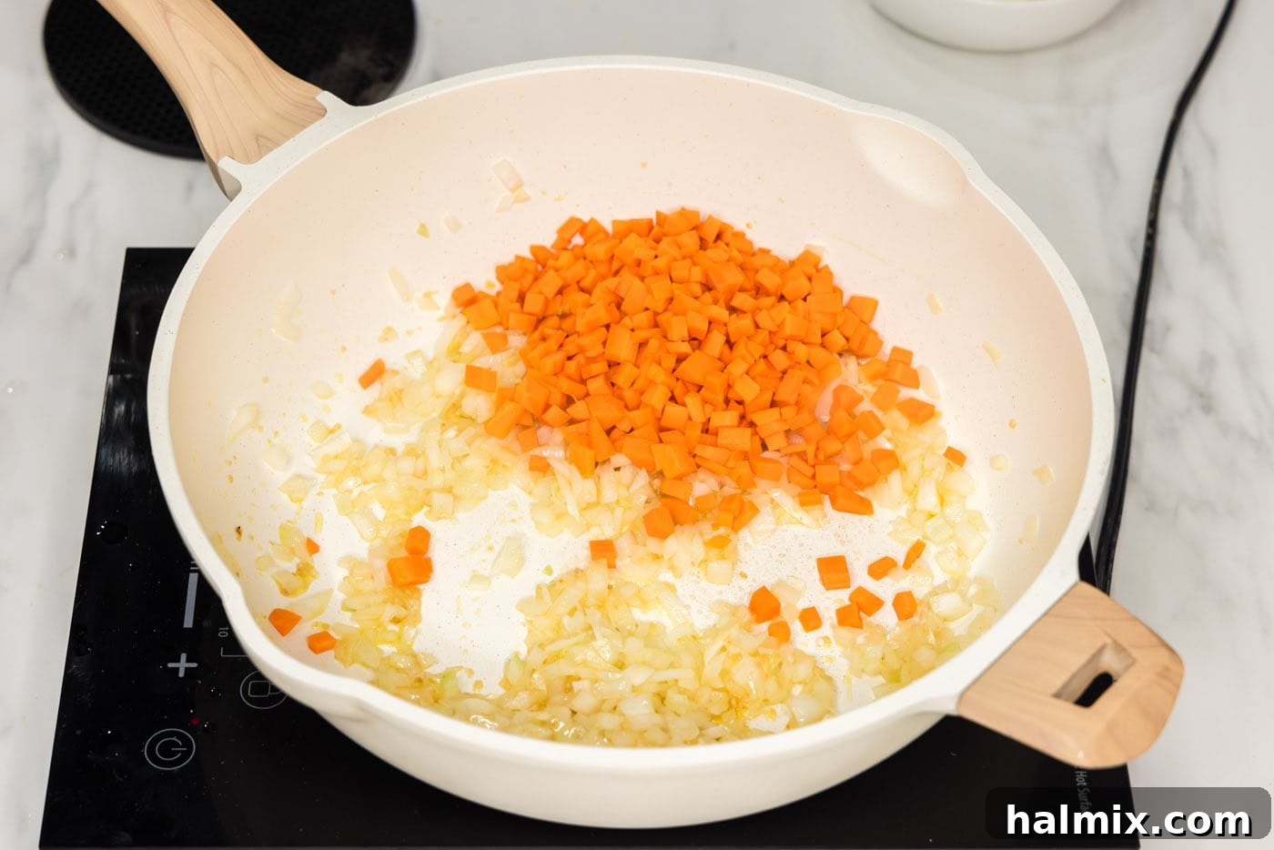 Diced carrots added to a skillet with onion, garlic, and ginger, being stir-fried.