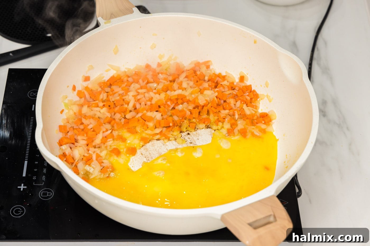 Whisked eggs being added to one side of a skillet, next to stir-fry vegetables.