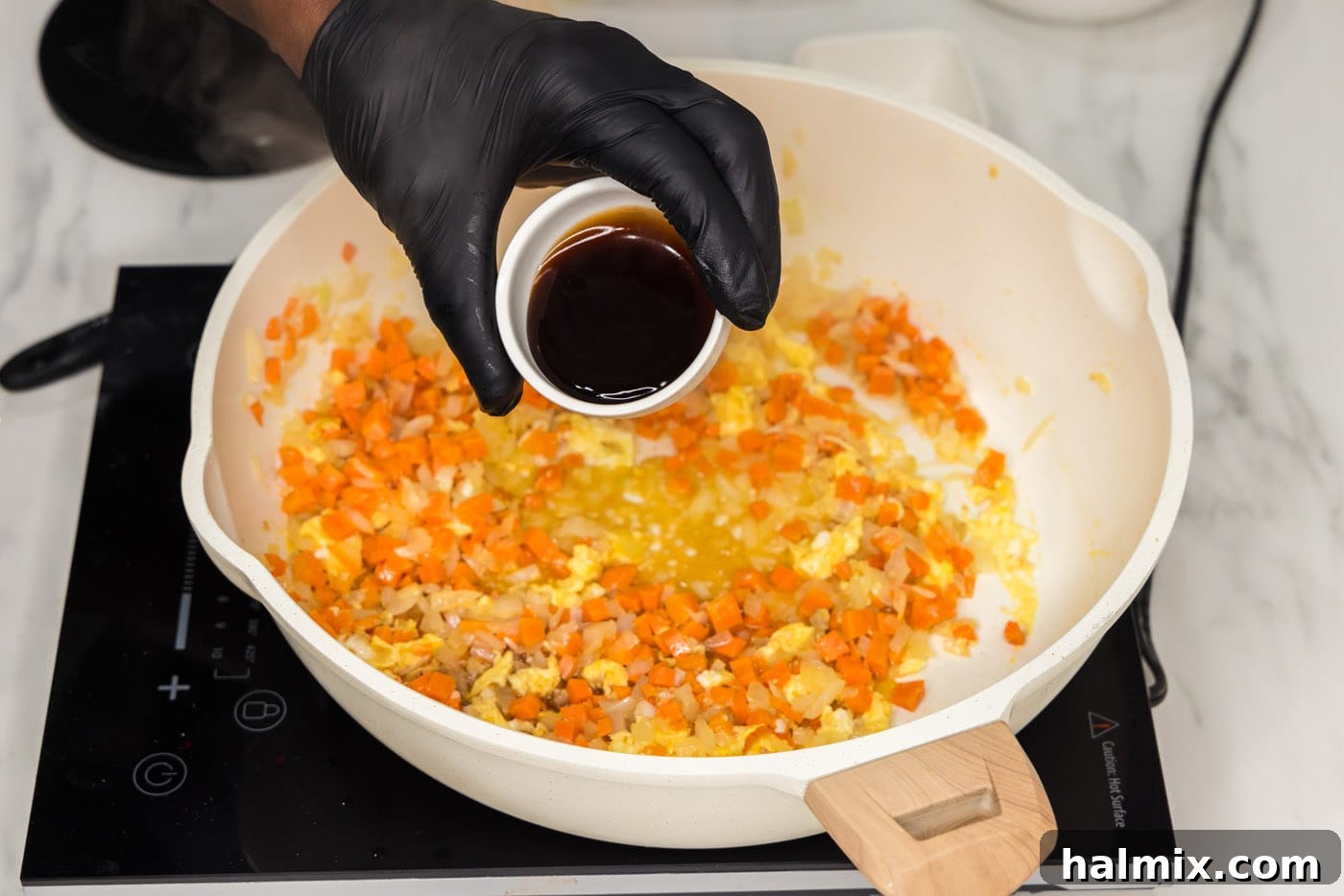 Oyster sauce being added to a skillet containing egg and vegetables, ready to be mixed.