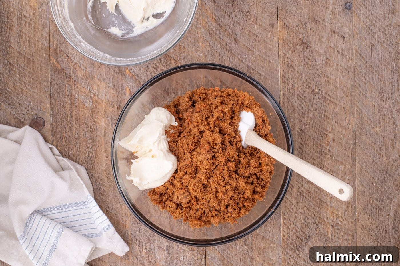 Cream cheese frosting being mixed into crumbled carrot cake, forming a cohesive mass