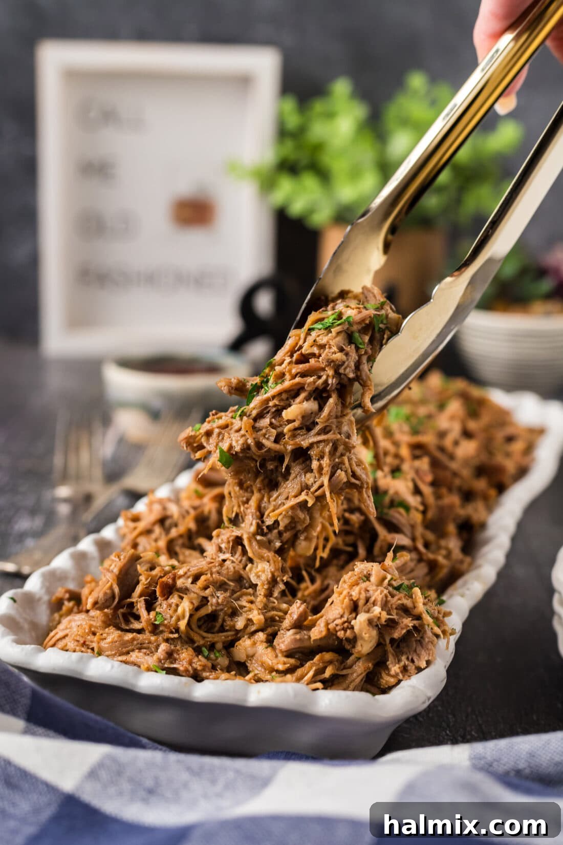 Tongs holding up perfectly shredded pulled pork above a platter