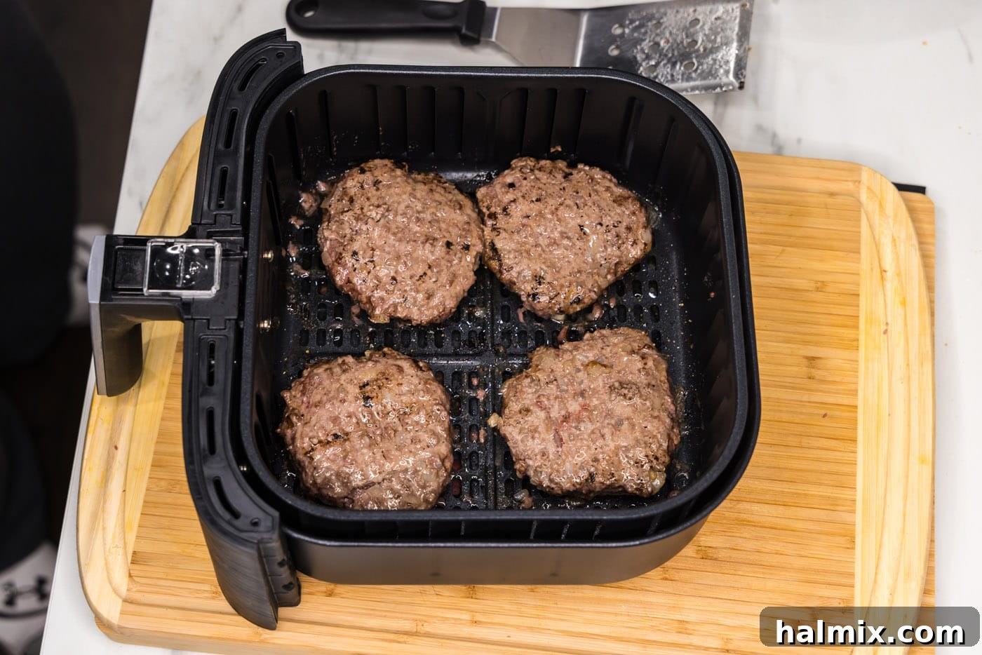 Fully cooked burger patties resting in the air fryer basket, displaying a beautiful golden-brown sear.
