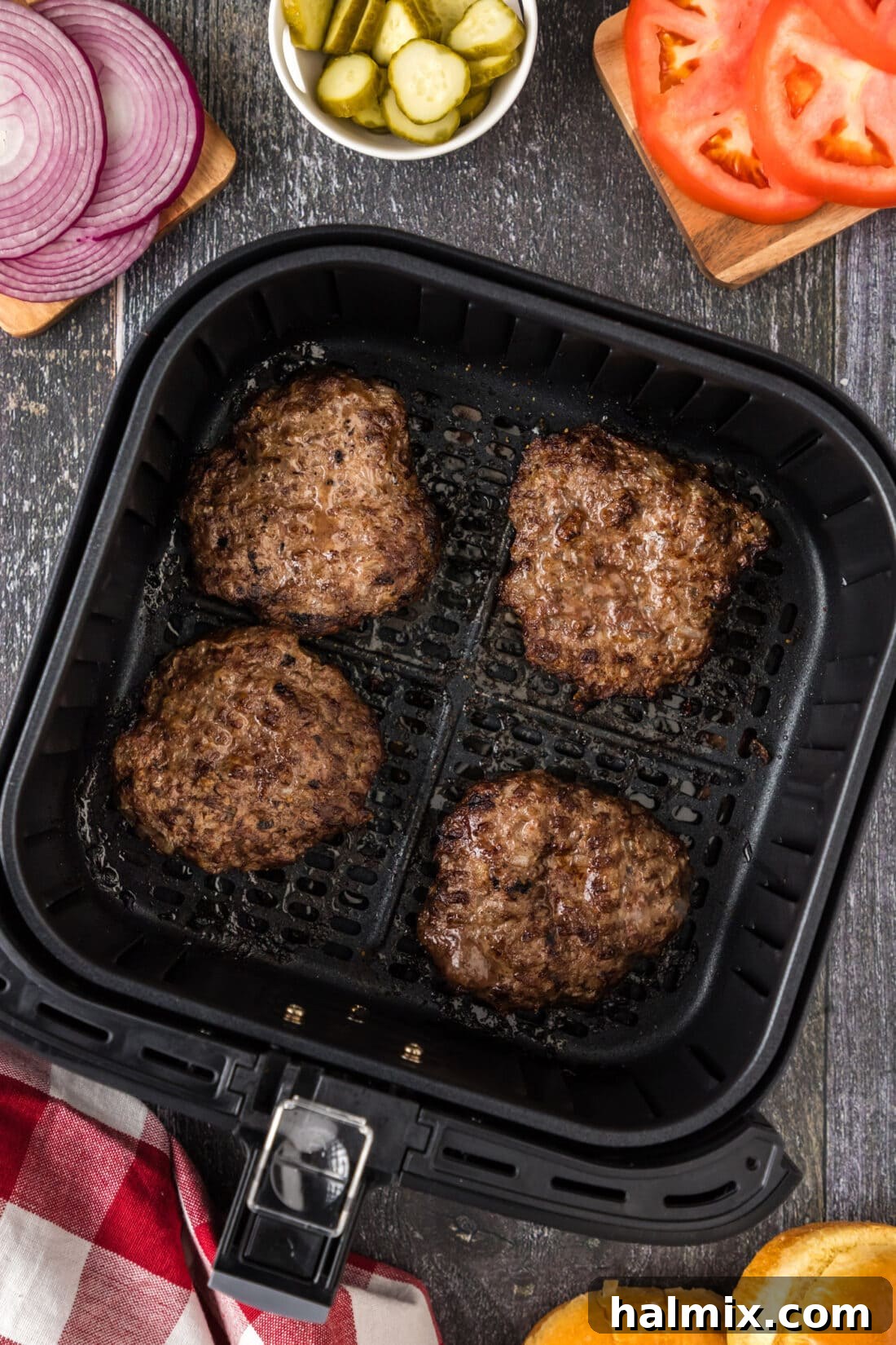 Four perfectly browned air fryer burgers arranged in an air fryer basket, ready to be removed and served.