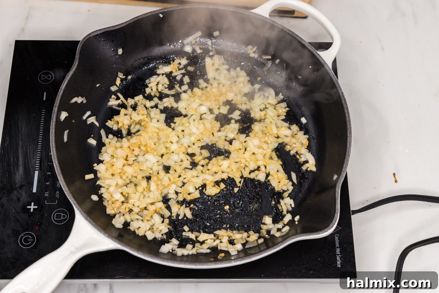 A close-up shot of minced onion and garlic being sautéed in olive oil in a large skillet, releasing their aromas.