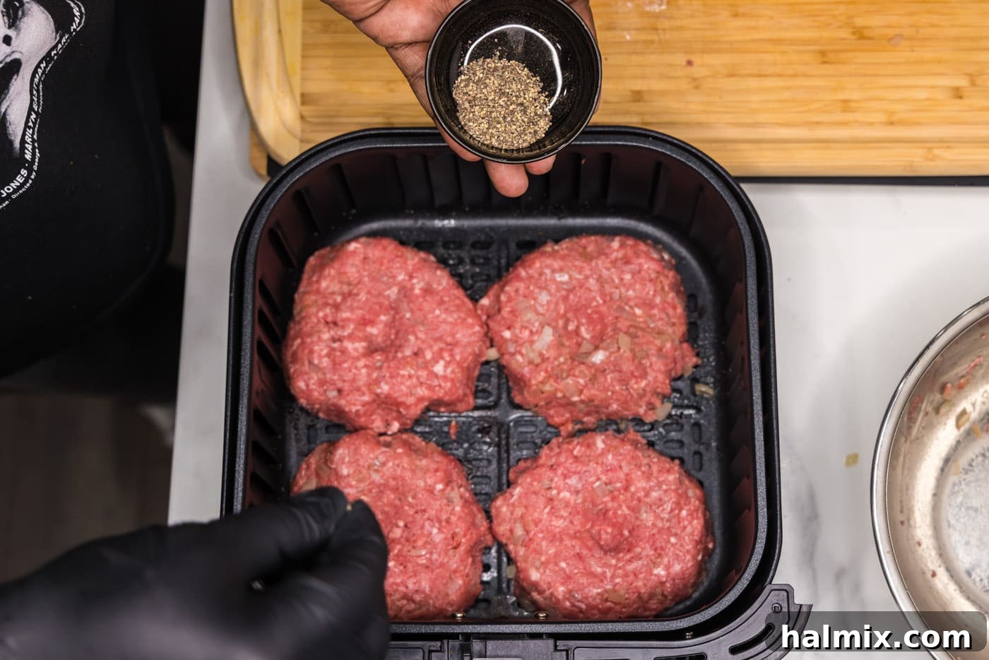Freshly ground black pepper being sprinkled over burger patties resting in the air fryer basket.