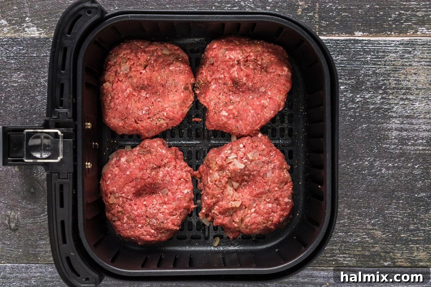 Four seasoned burger patties neatly arranged in a single layer within the air fryer basket, ready for cooking.