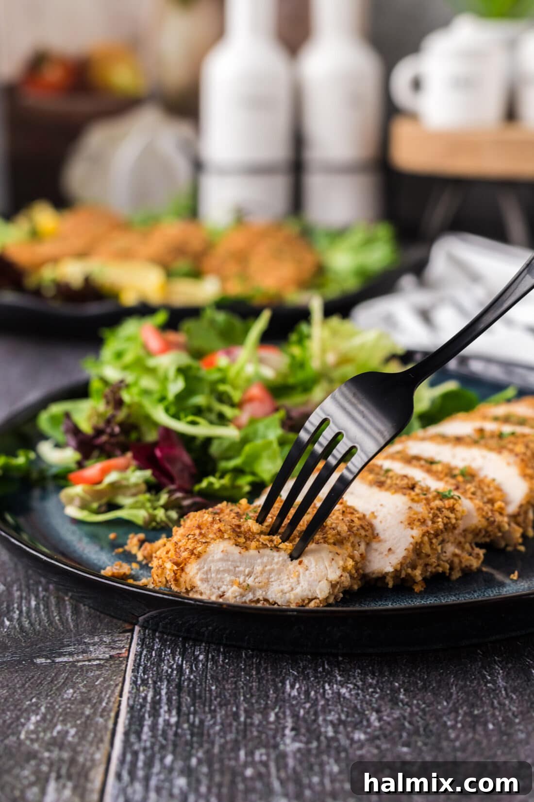 A fork piercing a piece of Almond Crusted Chicken, served with a fresh green salad on the side.