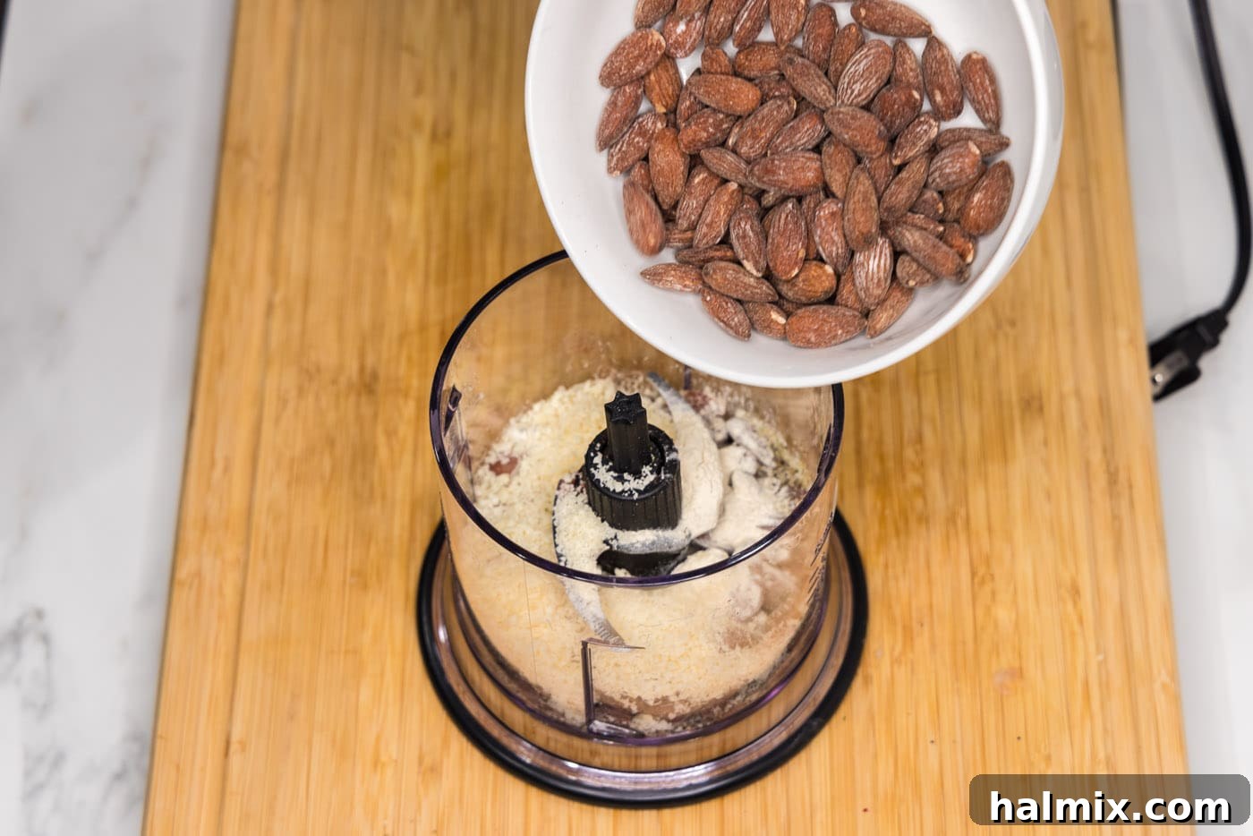 Pouring almonds into a food processor with seasonings and Parmesan cheese.
