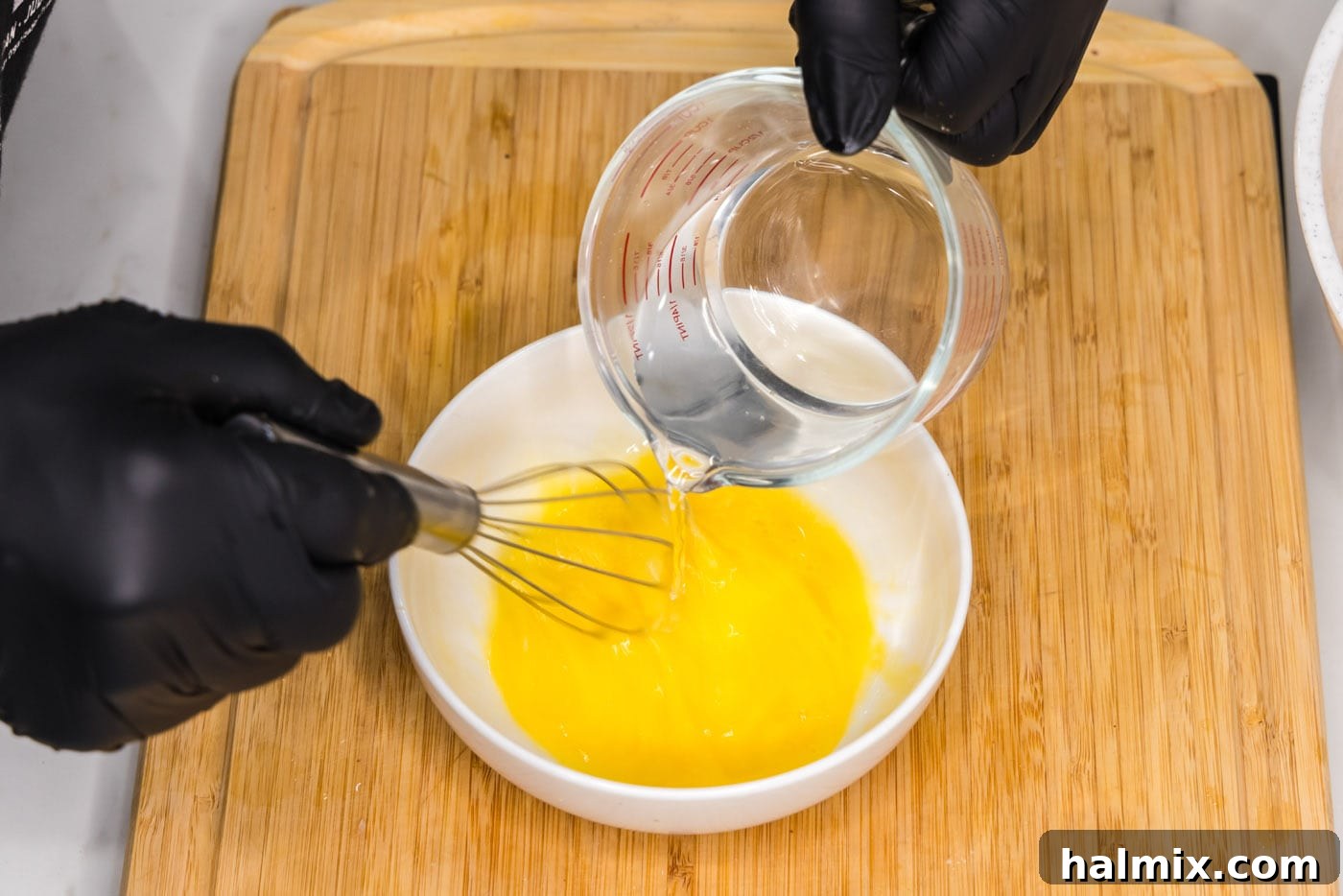 Whisking an egg with water in a bowl to create the egg wash for the chicken.