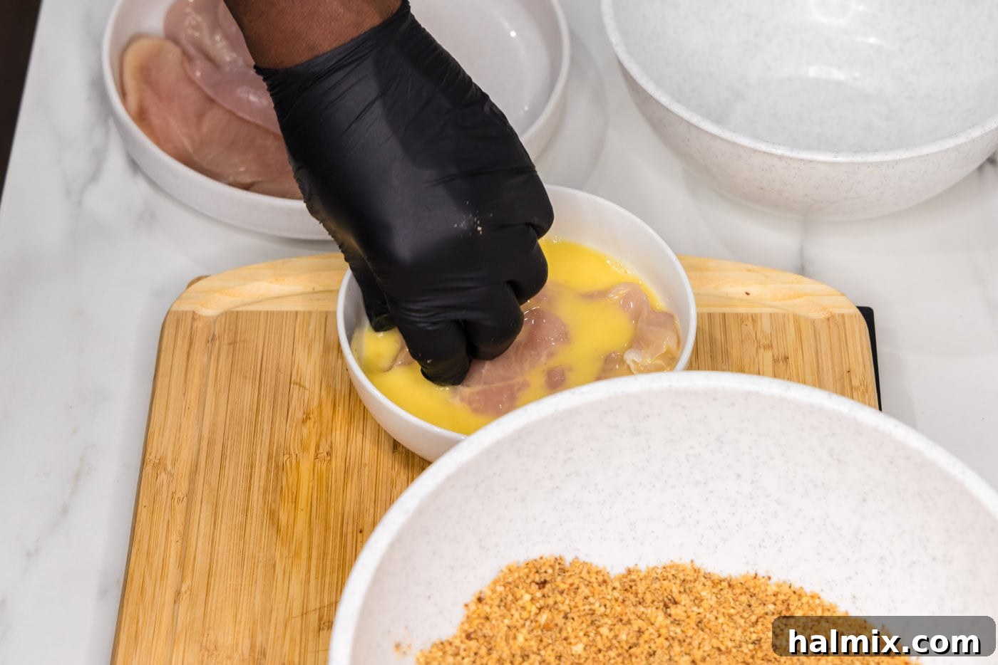 Dipping a chicken breast into the prepared egg wash.