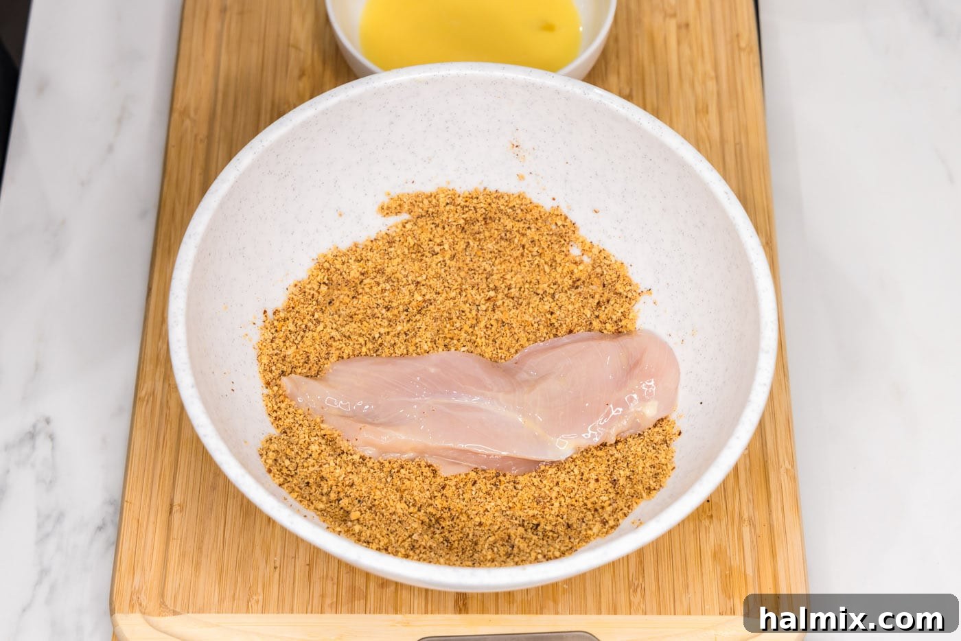 Dredging a chicken breast in the crushed almond and seasoning mixture.