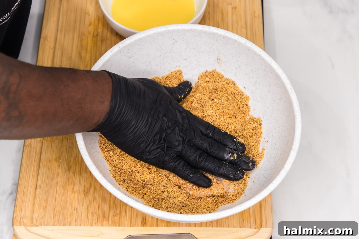 A hand gently patting the almond breading onto a chicken breast, ensuring it adheres well.