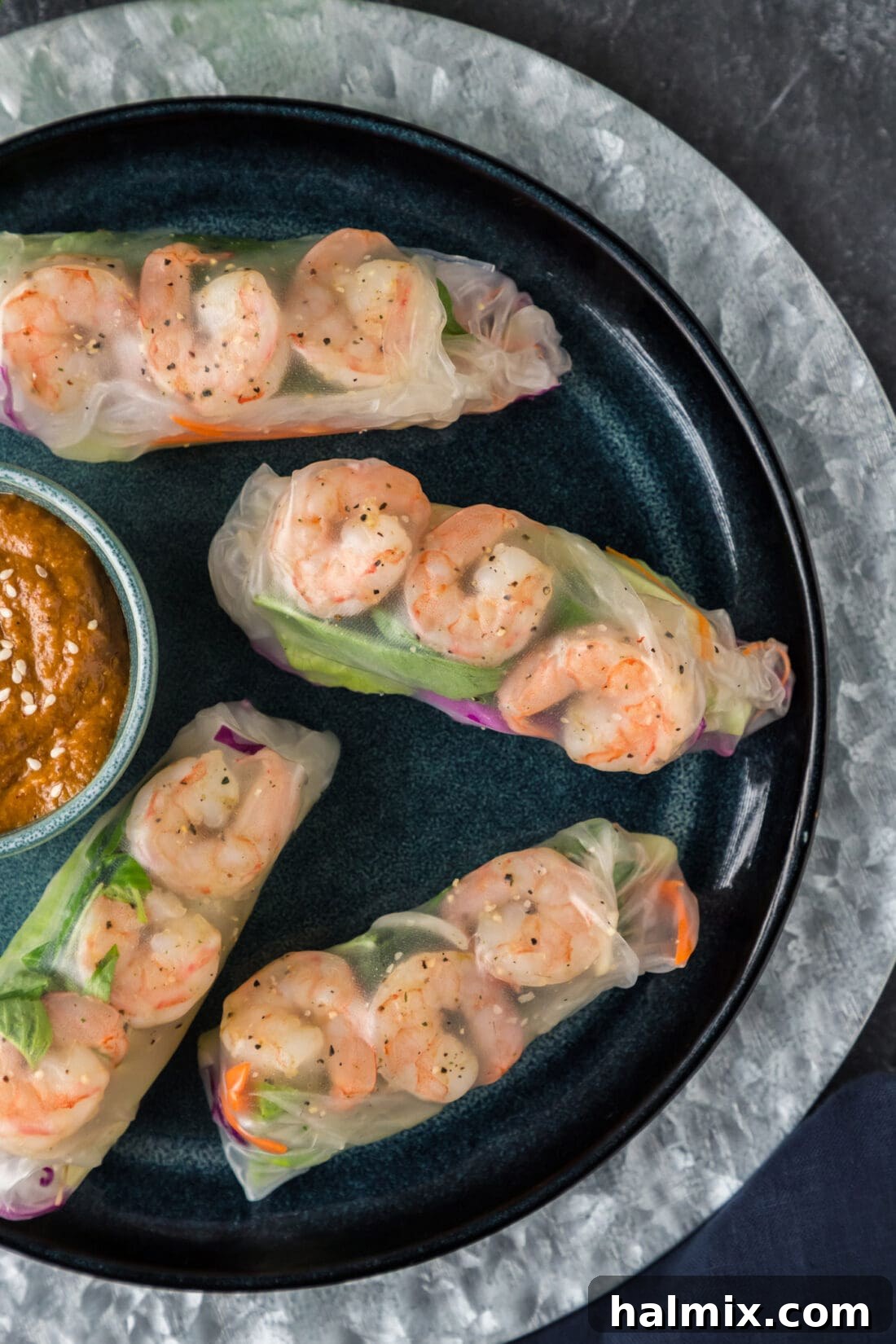 Close up overhead photo of Shrimp Spring Rolls on a plate. The rolls are perfectly wrapped, showcasing the vibrant fillings like pink shrimp, green lettuce, and red cabbage through the translucent wrapper. They are arranged neatly on a white plate, ready to be served.