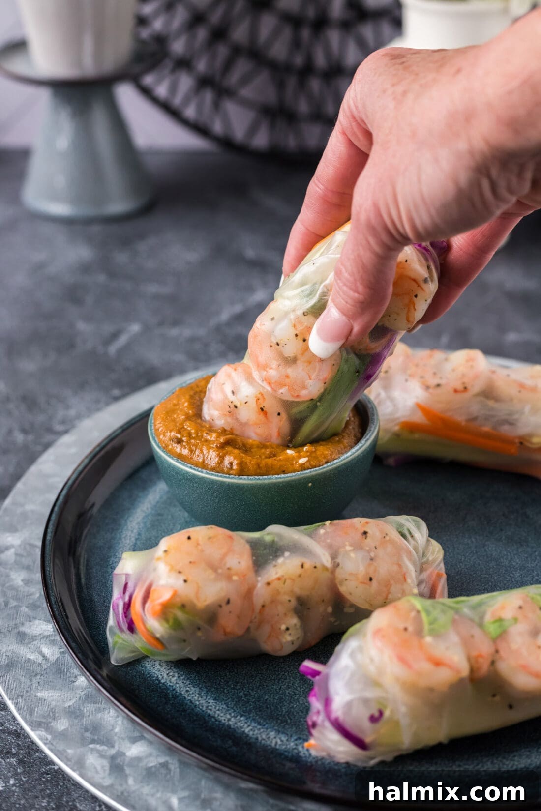 A perfectly wrapped Shrimp Spring Roll being dipped into a small, elegant bowl of rich peanut sauce, highlighting its readiness for a flavorful bite. The fresh ingredients are visible through the translucent wrapper.