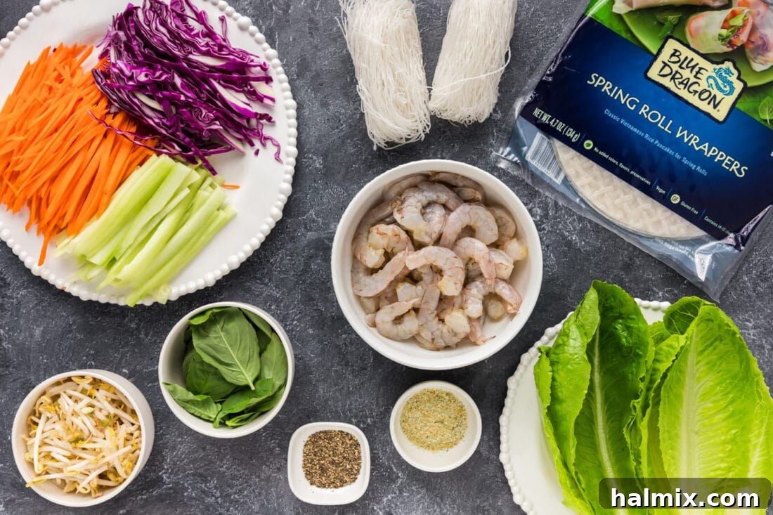 A flat lay photograph showcasing all the fresh, colorful ingredients for Shrimp Spring Rolls arranged neatly on a light surface. Ingredients include raw shrimp, fresh basil, romaine lettuce, red cabbage, carrots, celery, bean sprouts, bean thread noodles, and a package of spring roll wrappers.