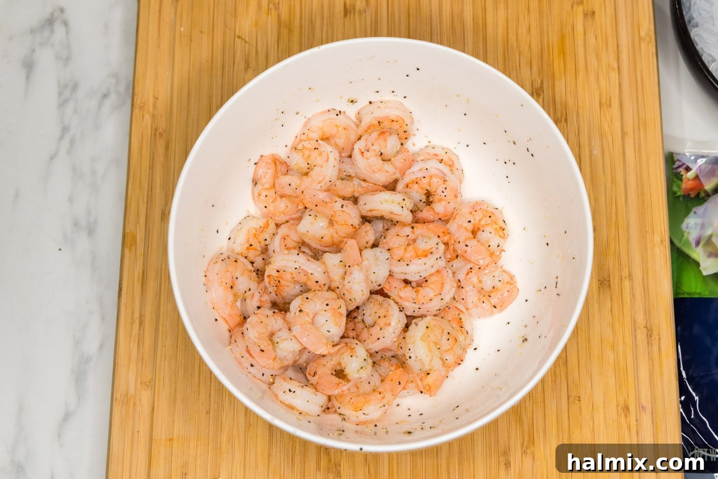 cooked shrimp in a bowl, seasoned with garlic salt and pepper, ready to be tossed. The shrimp are bright pink and plump.