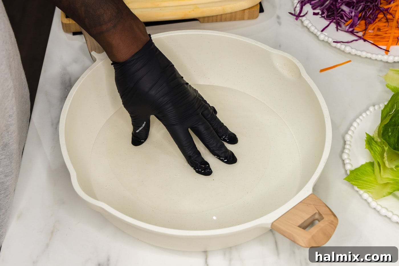 a spring roll wrapper being dipped into a skillet of water to soften, shown partially submerged in the water.