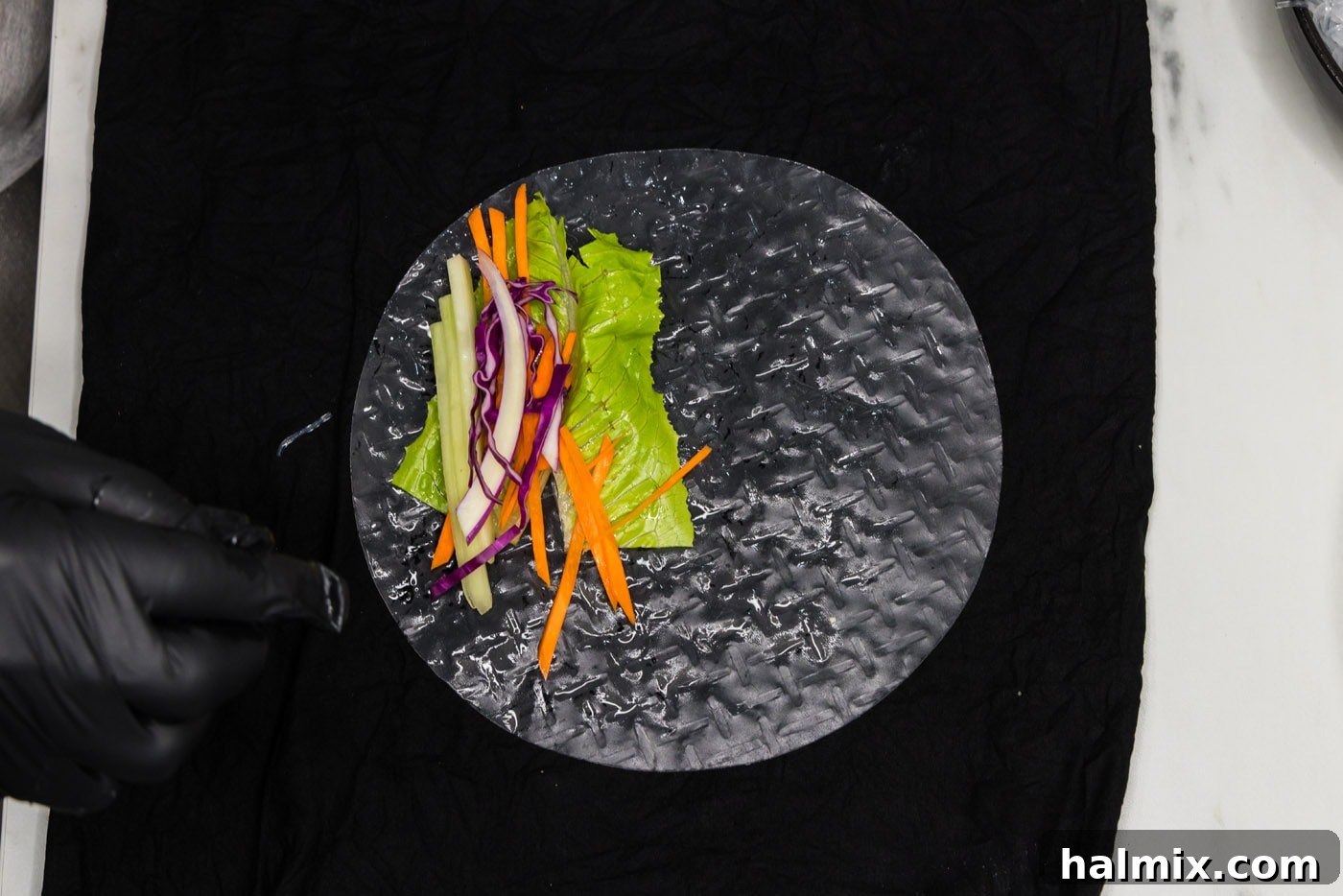 carrots, lettuce, and cabbage being added to a spring roll wrapper laid on a damp surface, forming the initial layer of the filling.