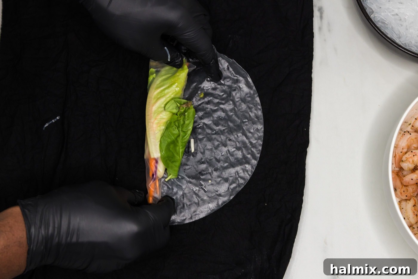 wrapping vegetables in a spring roll wrapper, with the bottom half rolled up and the filling visible.