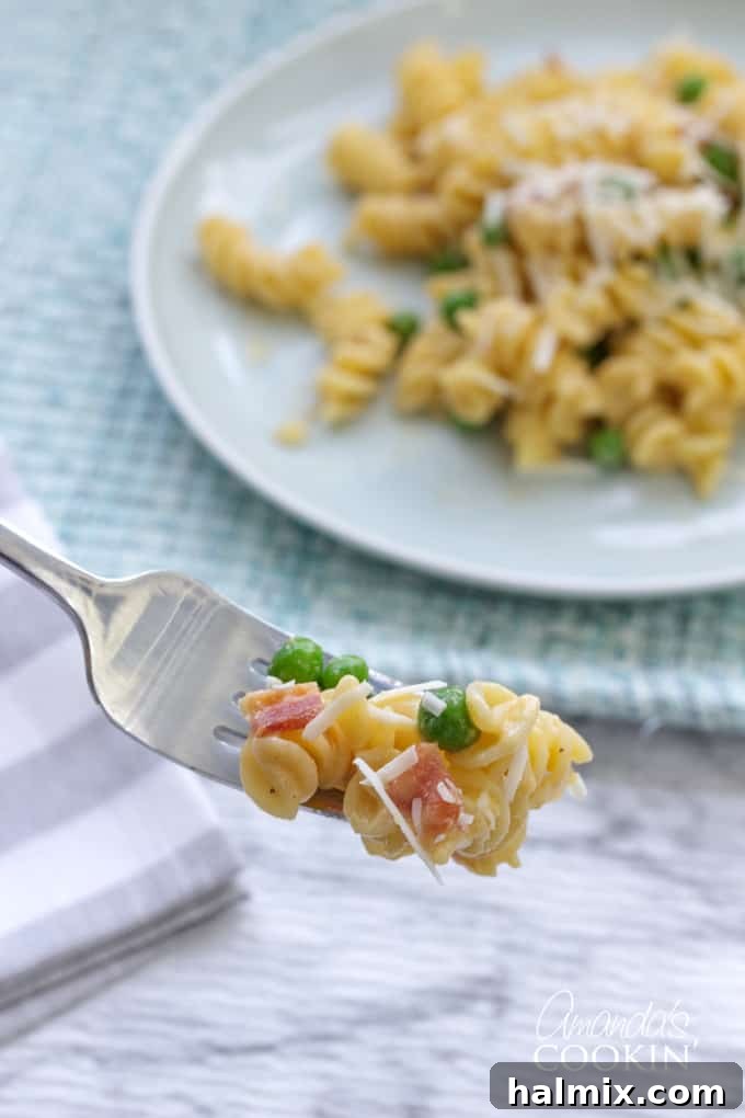 A forkful of Rotini with Peas and Cheese, showing the creamy texture and individual peas and bacon pieces.