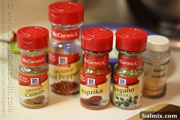 Hearty Chicken Chili with Black Beans and Sweet Corn 5 A close-up view of essential McCormick spice bottles, featuring ground cumin, crushed red pepper, paprika, and oregano leaves.
