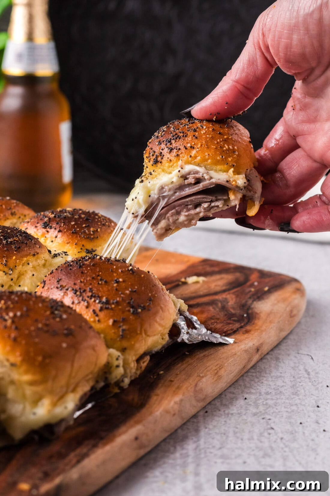 Hand pulling up a Roast Beef Slider from a board with a cheese pull, showcasing gooey mozzarella